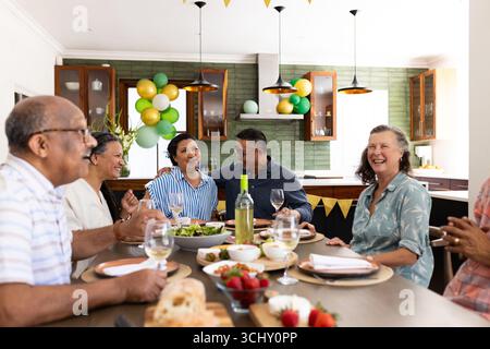Verschiedene Seniorenfreunde genießen eine lebhafte Dinner-Party, teilen Lachen und Gespräche, zu Hause Stockfoto