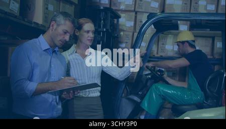 Mit Klemmbrett und Stift, zwei Kollegen zeigen auf den Lagerbestand im Lager, mit Gabelstapler Stockfoto