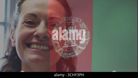 Lächelnde mittelerwachsene Frau, die Zähne auf einer digitalen Afghanistan-Flagge zeigt, mit Emblem, Kopierraum Stockfoto