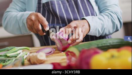 Indischer Koch mit Schürze, schneidet rote Zwiebeln auf Schneidebrett in der Küche, mit Paprika Stockfoto