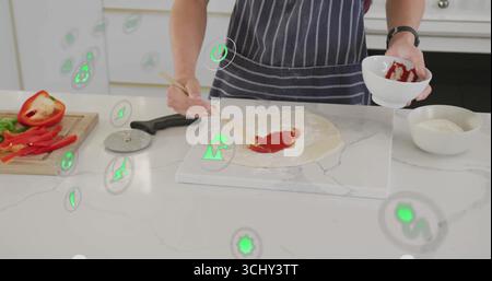Teenager mit gestreifter Schürze und Tomatensauce auf Pizzateig auf der Küchentheke mit Spachtel verteilen Stockfoto