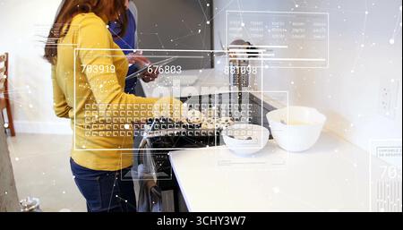 Kochende Paare mit Gasherd in der modernen Küche, Frau brät Essen und Mann liest Tablette Stockfoto