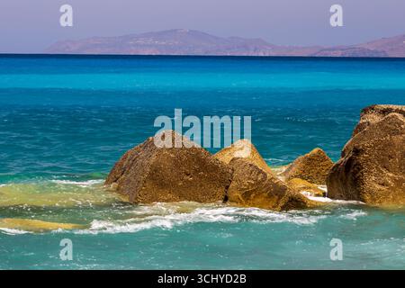 Felsige Küste mit klarem blauem Meer und fernen Bergen unter sonnigem Himmel Stockfoto