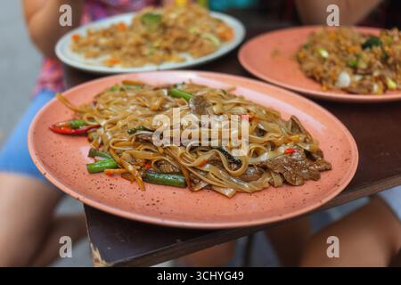 Auf einem geschäftigen thailändischen Straßenmarkt genießen Sie tagsüber eine lebhafte Teller mit gebratenen Nudeln. Stockfoto