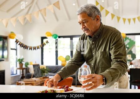 Senior Mann, der Essen zubereitete und Weinglas auf festlicher Hausfeier hielt Stockfoto