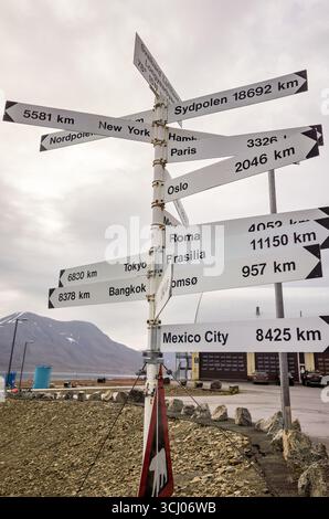 Longyearbyen Svalbard Airport Wegweiser zu Global Cities Longyearbyen Norwegen // LONGYEARBYEN, Svalbard — Ein Wegweiser am Flughafen Svalbard Longyearbyen, befindet sich bei 78° 15' N und zeigt Entfernungen zu verschiedenen globalen Städten an. Das Schild weist darauf hin, dass Sydpolen 18.692 Kilometer (11.590 Meilen) und der Nordpol 5.581 Kilometer (3.468 Meilen) entfernt ist. Weitere aufgelistete Reiseziele sind New York, Hamburg, Paris, Oslo, Rom, Brasilia, Tokio, Bangkok, Tromsø und Mexiko-Stadt, mit Entfernungen von 957 km (595 Meilen) bis 11.150 km (6.928 Meilen). Dieser Flughafen ist ein wichtiges Tor zu den Arcti Stockfoto