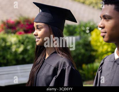 Absolventen verschiedener Studenten in Mützen und Kleidern, lächeln im Garten und feiern Erfolge Stockfoto