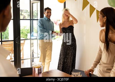 Verschiedene Freunde überraschen Frau mit Geburtstagsfeier zu Hause und teilen fröhliches Lachen Stockfoto