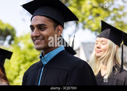 Verschiedene Absolventen in Mützen und Kleidern feiern mit fröhlichem Lächeln den Erfolg im Garten Stockfoto