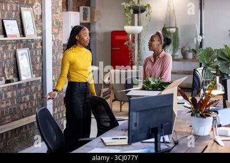 Zwei Frauen diskutieren über das Projekt in einem modernen Büro mit Werken und offenem Arbeitsplatz Stockfoto