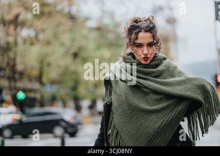 Stilvolle Frau im grünen Schal, die draußen auf einer lebhaften Stadtstraße posiert Stockfoto