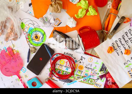 Unordentlicher Arbeitsplatz, chaotisches Büro, überarbeitet, Frist, Stress, Bürokratiekonzept mit unangenehmem Schreibtisch und verschiedenen Kalenderblättern und Papierkram Stockfoto
