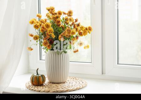 Strauß von herbstlichen orangen Blumen in weißer Vase und Kürbis auf Fensterbank. Gemütliches Zuhause und ruhig. Nahaufnahme. Stockfoto