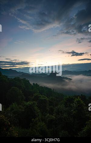Aus der Vogelperspektive der Sonne über den Berggipfeln scheint durch das Tal. Bewölkter Himmel und umliegende Hügel unterstreichen das friedliche Ambiente Stockfoto