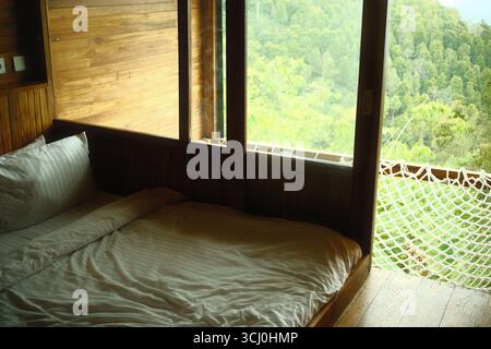 Ein Schlafzimmer mit Holzkabine mit einer Hängematte am Fenster in den bewaldeten Hügeln Stockfoto