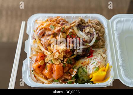 Blick von oben auf einen hawaiianischen Poke-Mittagstisch mit scharfem Aahi, Lachs, Kalua-Schweinefleisch, Krabbensalat und eingelegtem Gemüse. Saubere Präsentation Stockfoto