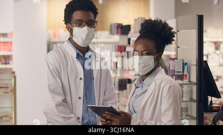 Ärzte in Masken covid Gesundheitswesen Apotheke Berater Ärzte mit digitalen Tabletten Medizin Pillen Medikamenten Inventar männliche weibliche Apotheker afrikanisch Stockfoto