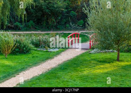 Pfad, der im August zur roten Brücke über den Bourne Stream bei Coy Pond Gardens, Bournemouth, Dorset, Großbritannien führt Stockfoto