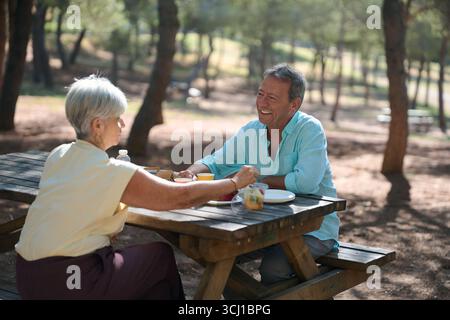 Glückliches Seniorenpaar genießt Picknick-Mittagessen im sonnigen Waldpark Stockfoto
