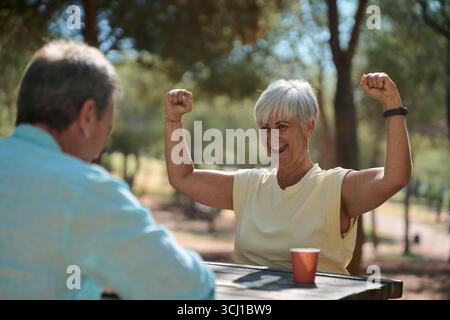 Glückliche Seniorin gewinnt ein Dominospiel im Park Stockfoto
