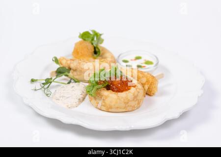 Elegantes Servieren von Gourmet-Pfannkuchen mit rotem Kaviar, frischem Salat, Cremesauce und Kräutern auf einem weißen Teller für das Restaurantmenü. Stockfoto