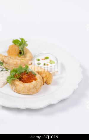 Elegantes Servieren von Gourmet-Pfannkuchen mit rotem Kaviar, frischem Salat, Cremesauce und Kräutern auf einem weißen Teller für das Restaurantmenü. Stockfoto