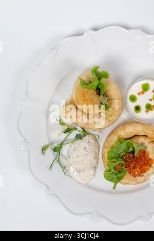 Elegantes Servieren von Gourmet-Pfannkuchen mit rotem Kaviar, frischem Salat, Cremesauce und Kräutern auf einem weißen Teller für das Restaurantmenü. Stockfoto