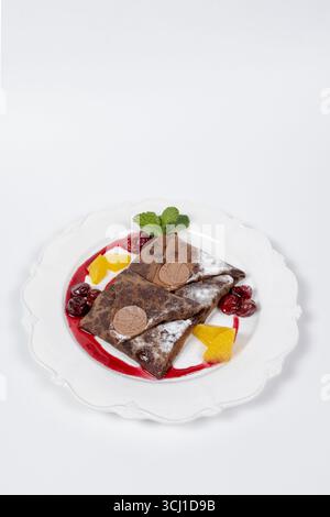 Köstliche Schokoladenkrepes mit Kirschen, Orangenscheiben, Minzblättern, Schokoladendekoration und Puderzucker. Perfekt für das Restaurantmenü, Dessertwerbung Stockfoto