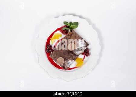 Leckere Schokoladenkrepes mit Kirschen, Orangenscheiben, Minzblättern und Schokoladenabdeckung, von oben erfasst. Perfekt für Restaurantmenüs, Anzeigen oder Essen Stockfoto