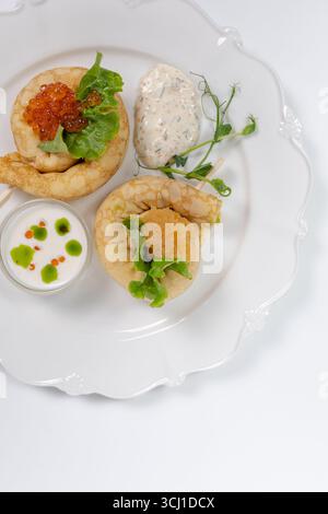 Elegantes Servieren von Gourmet-Pfannkuchen mit rotem Kaviar, frischem Salat, Cremesauce und Kräutern auf einem weißen Teller für das Restaurantmenü. Stockfoto