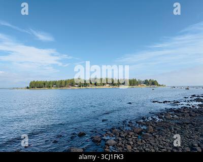 Ruhige Küstenlandschaft mit einer Insel mit üppigen Bäumen unter einem klaren blauen Himmel. Stockfoto