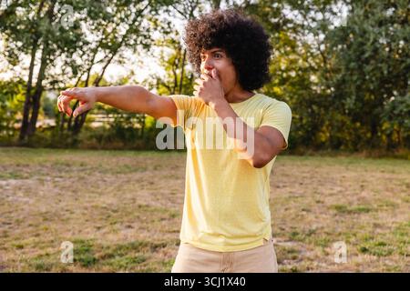 Schockierter junger Mann, der mit dem Finger nach draußen in einem Park zeigt Stockfoto