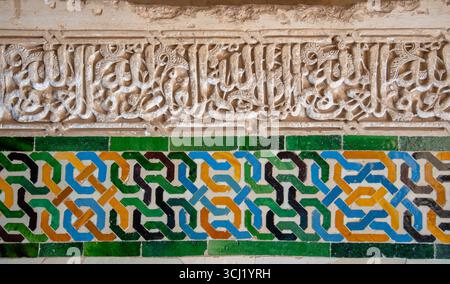 La Alhambra, Spanien - 12. März 2025: Detaillierte Wand mit geometrischen Fliesenmustern in lebhaften Farben und geschnitzten islamischen Inschriften aus dem Koran. Stockfoto