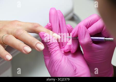 Nagelstylist, der Maniküre macht. Weibliche Hand-Schönheitspflege. Professionelle Nagelstudio-Behandlung. Pinkfarbene Handschuhe und Maniküre. Frau Hand Nahaufnahme mit Nagel. Stockfoto