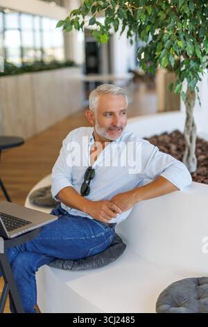 Ruhiger reifer Geschäftsinhaber im Büro, selbstbewusster grauhaariger Mann in entspannter Pose Stockfoto