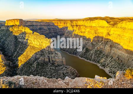 Ein atemberaubender Panoramablick auf einen goldenen Sonnenuntergang vom Devil's Canyon Overlook, der einen warmen Glanz über die dramatische Landschaft des Bighorn Canyon wirft Stockfoto