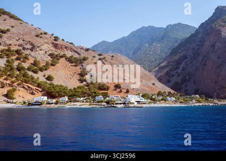 Agia Roumeli Dorf am Fuße der steilen zerklüfteten Berge entlang der Südwestküste der Insel Kreta, Griechenland. Blick vom Boot, das sich der Villa nähert Stockfoto