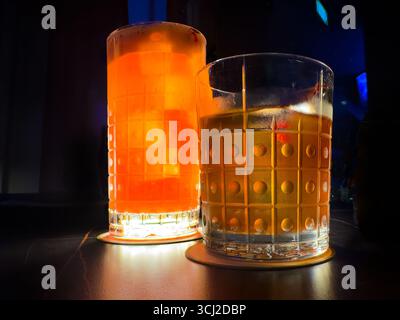 Nahaufnahme von 2 Cocktails Singapore Sling & Old Fashioned in gemusterten Gläsern, schummrig beleuchtete Tische, Atmosphäre des Singapore Atico Lounge & Bar ION Orchard Stockfoto