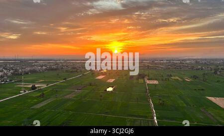 Sonnenaufgang über grünen landwirtschaftlichen Feldern in der Nähe des Nils in Luxor, Ägypten, mit Ackerland und leuchtendem Himmel am Horizont. Stockfoto