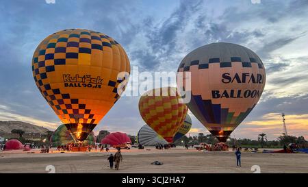 Luxor, Ägypten - 10. Februar 2025: Bunte Heißluftballons werden vor Sonnenaufgang aufgeblasen, Flammen beleuchten die Szene und Touristen bereiten sich auf den Flug vor Stockfoto