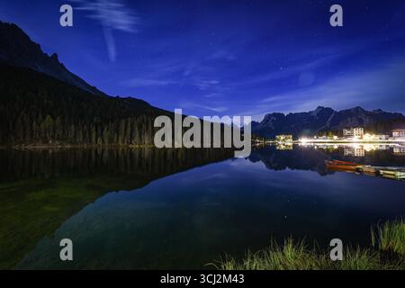 Ein atemberaubendes Langzeitfoto des Lago di Misurina bei Nacht. Der tiefblaue Sternenhimmel und die beleuchteten Gebäude und Hotels am fernen Ufer A Stockfoto