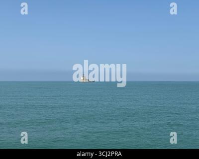 Silhouetten von Fracht- und Kreuzfahrtschiffen am fernen Horizont in der Bucht von Cádiz, mit ruhigem Atlantik und klarem Sommerhimmel nahe dem geschäftigen p Stockfoto