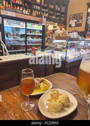 Gemütliches Interieur der traditionellen spanischen Tapas-Bar in Cadiz, mit Holztheken, hängenden Schinken, bunten Fliesen, kleinen Tellern und Wein. Stockfoto