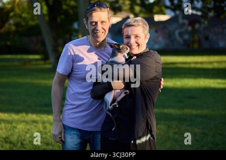 Ein fröhliches Paar mittleren Alters posiert mit seiner kanadischen Sphynx-Katze draußen in einem grünen Park. Das Foto spiegelt Liebe, Gemeinschaft und die Freude von sp. Wider Stockfoto