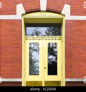 Blassgelbe Doppeltür mit Glaspaneelen, die von einer bogenförmigen roten Ziegelfassade in Chicago eingerahmt werden. Stockfoto