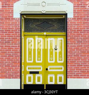 Verzierte gelbe Doppeltür mit dekorativen Paneelen, die von einer roten Ziegelfassade in Chicago eingerahmt werden. Stockfoto