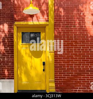 Gelb lackierte Industrietür mit Deckenlampe aus Metall an roter Backsteinwand in Chicago. Stockfoto