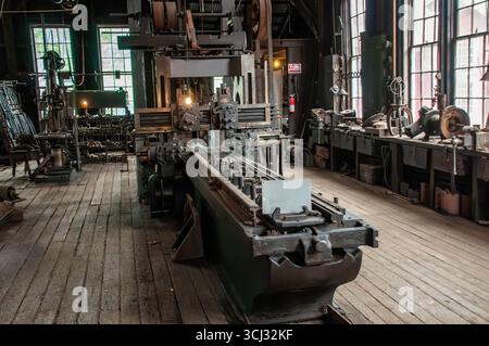 In einer historischen Werkstatt stehen große Vintage-Maschinen auf Holzböden. Sonnenlicht strömt durch hohe Fenster und beleuchtet die komplizierten Werkzeuge und Ausrüstungen, die für die Verarbeitung verwendet werden. Stockfoto