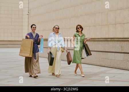 Drei Frauen gehen draußen mit Einkaufstaschen und lächeln Stockfoto