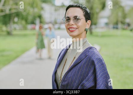 Porträt einer Frau mittleren Alters, die selbstbewusst im Stadtpark lächelt Stockfoto